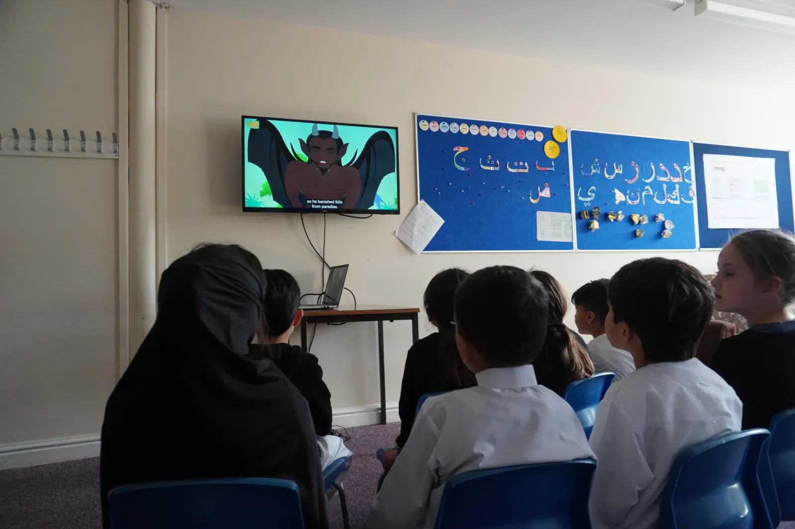 Children sitting on chairs watching a cartoon on a wall-mounted TV