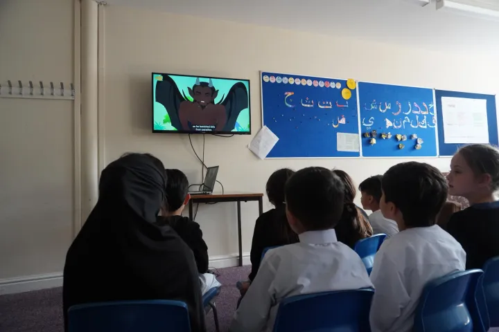 Children sitting on chairs watching a cartoon on a wall-mounted TV