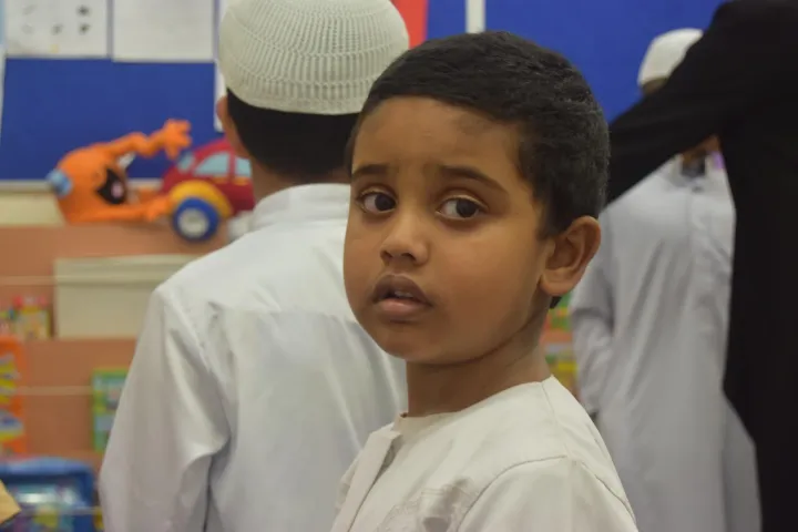 A child in a white cap at an assembly, looking over their shoulder