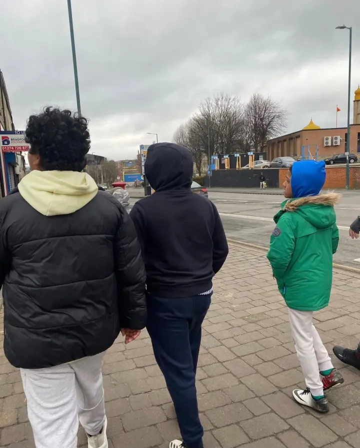 Children in coats walking together along a pavement, seen from behind