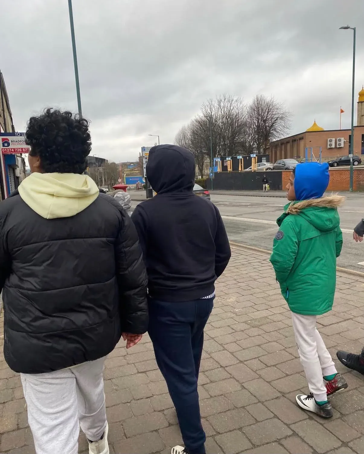 Children in coats walking together along a pavement, seen from behind