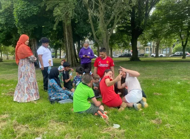 Children and staff sitting together on the grass in a park