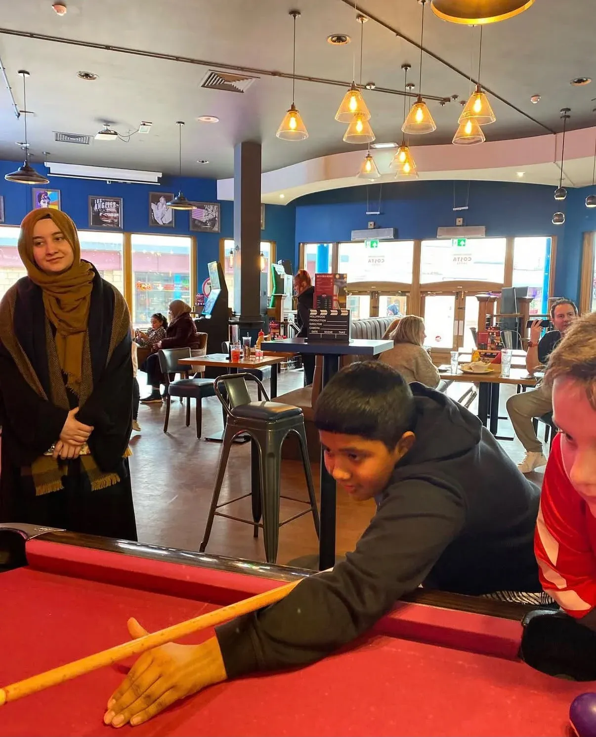 A child lining up a shot on a red pool table while an adult watches
